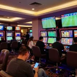 Engaging in kèo nhà cái betting strategies at a busy sports betting section of a casino.